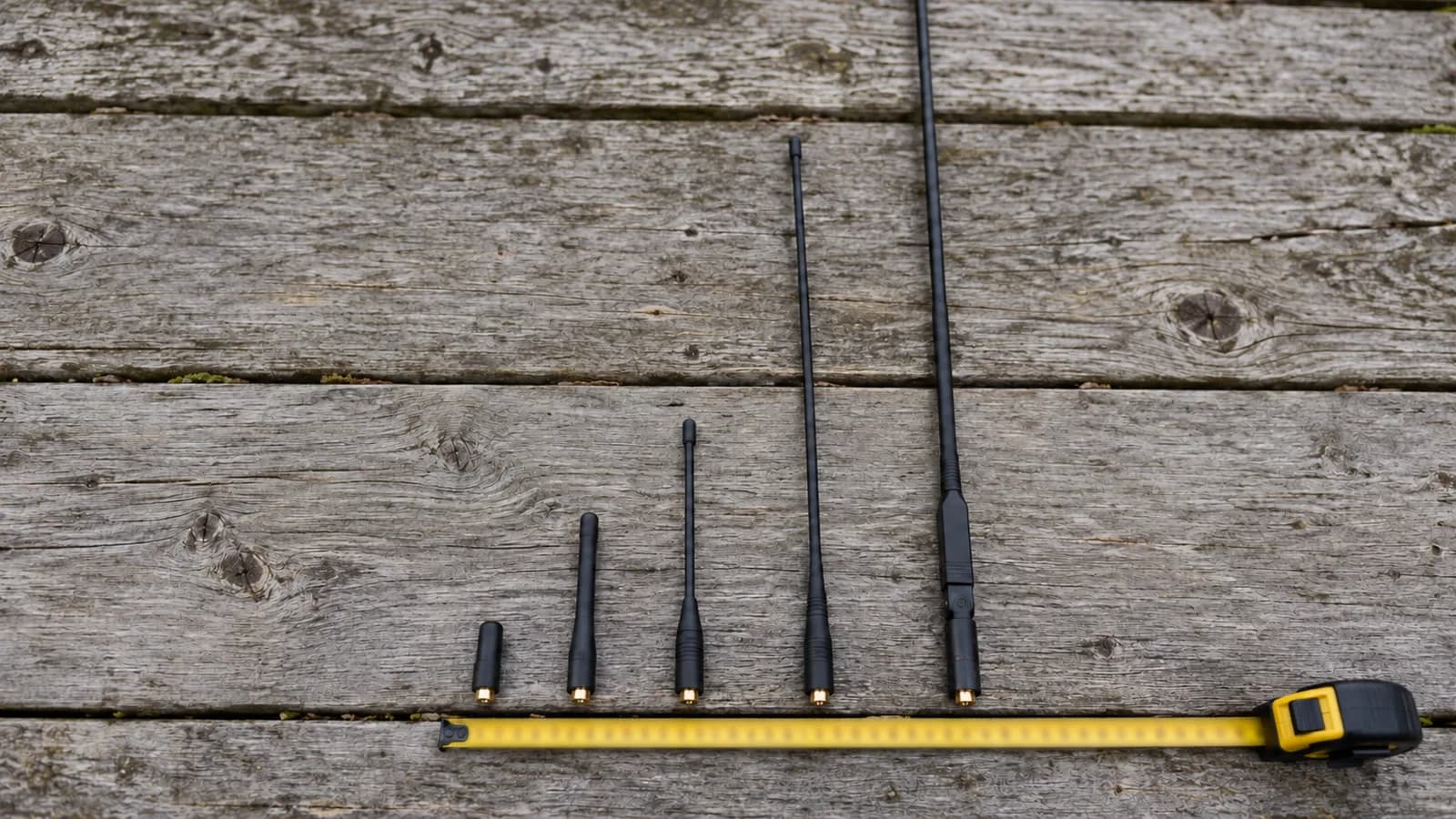 Several handheld ham antennas of very different lengths laid side by side along a tape measure